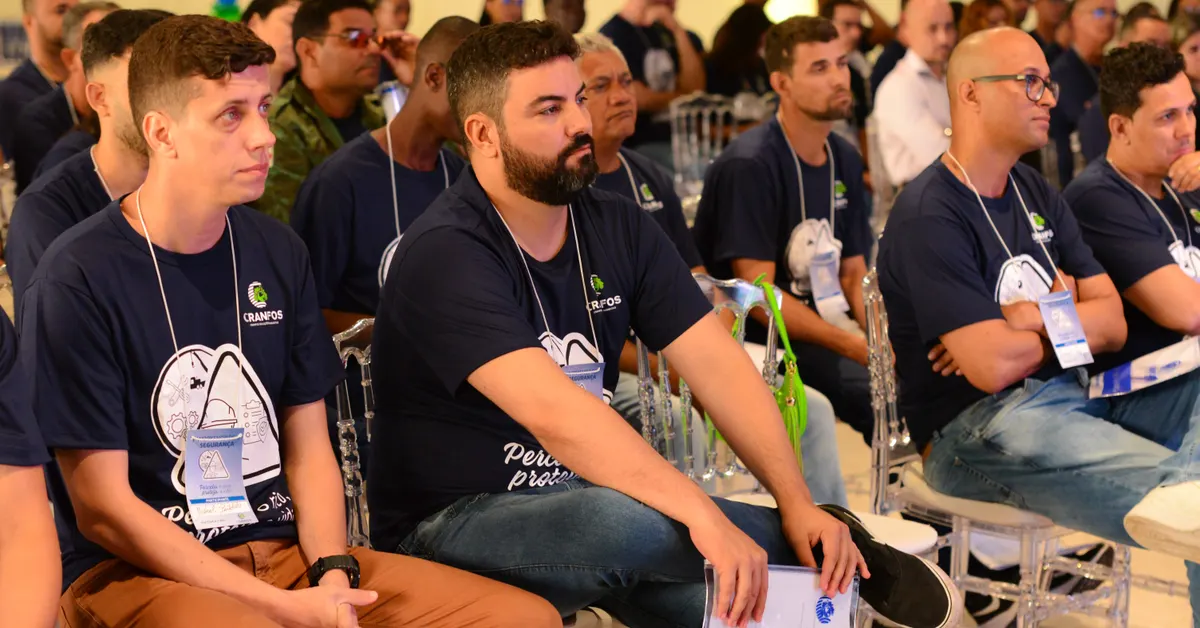 Plateia atenta durante uma palestra de SIPAT, com participantes usando camisetas do evento.