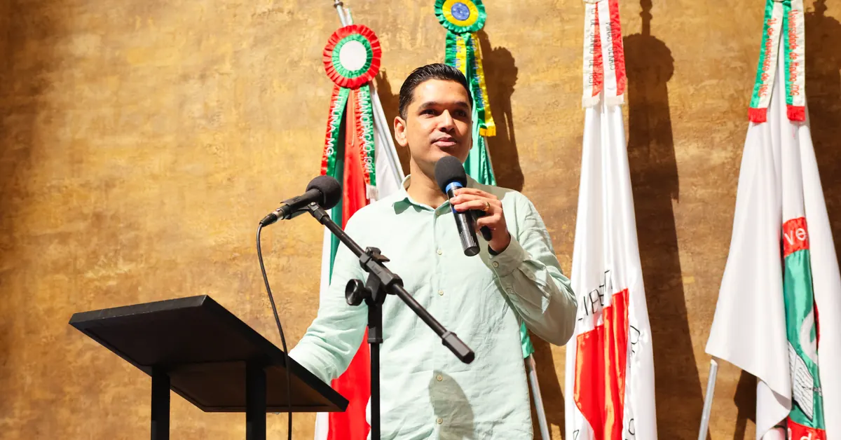 Deivson Lest conduz palestra ao microfone, diante de bandeiras